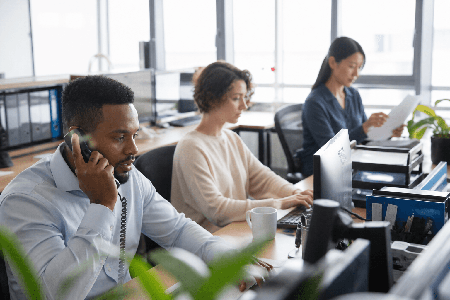 Three colleagues working at adjacent desks in a daylight office