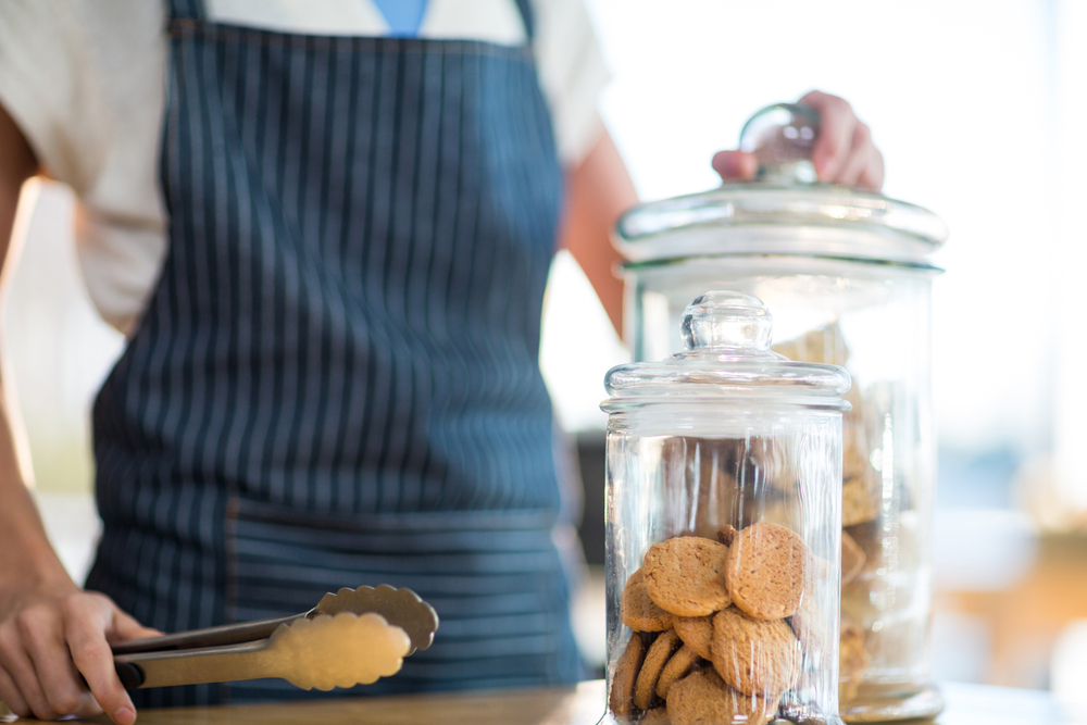 Two cookie jars, with a person holding tongs standing behind them