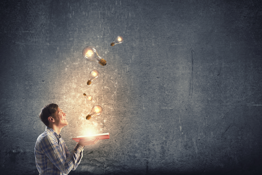 Lightbulbs flying out of a book that is open, sitting on a man's hands