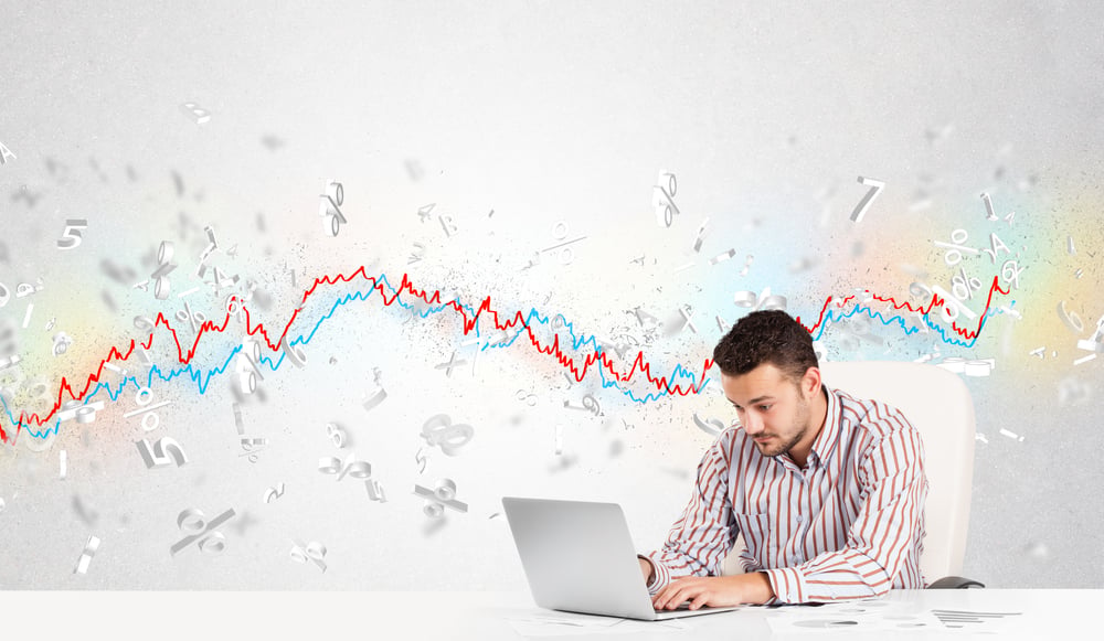 A man sitting at a laptop with a chart located behind him