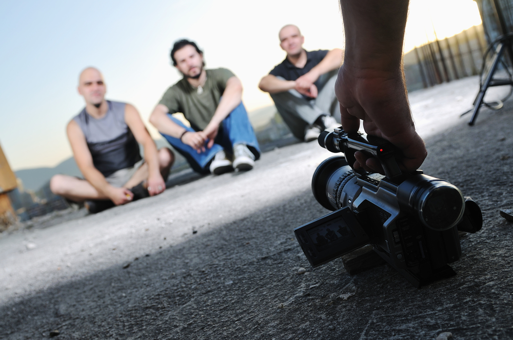 A video camera being placed on the ground, facing 3 people sitting down