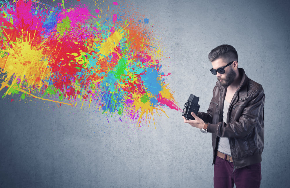 A retro hipster male taking photograph with a vintage camera of an urban wall with paint splatter concept