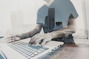 Man typing on a keyboard layered on top of a cityscape image