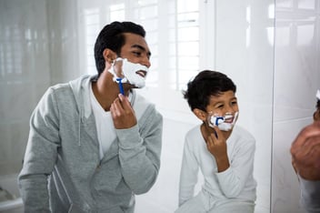 A father and young son shaving in the mirror